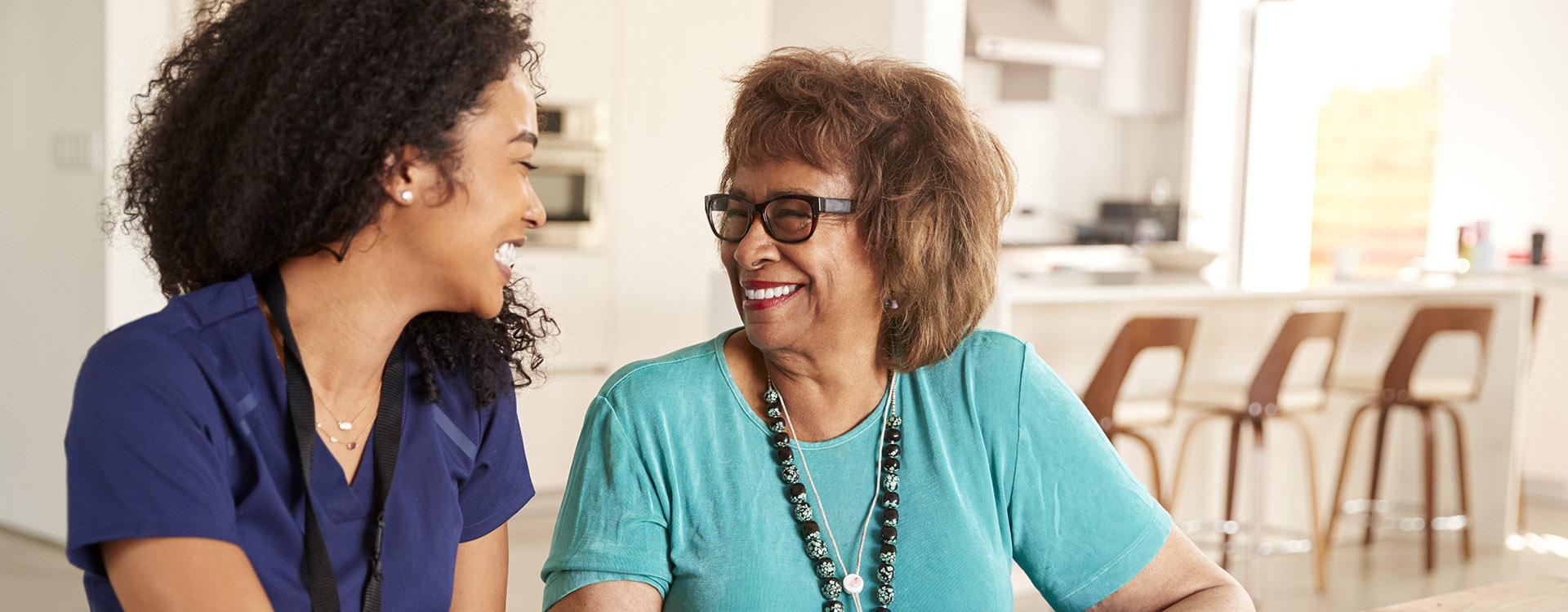 Female healthcare worker sitting at table smiling with a senior woman during a home health visit